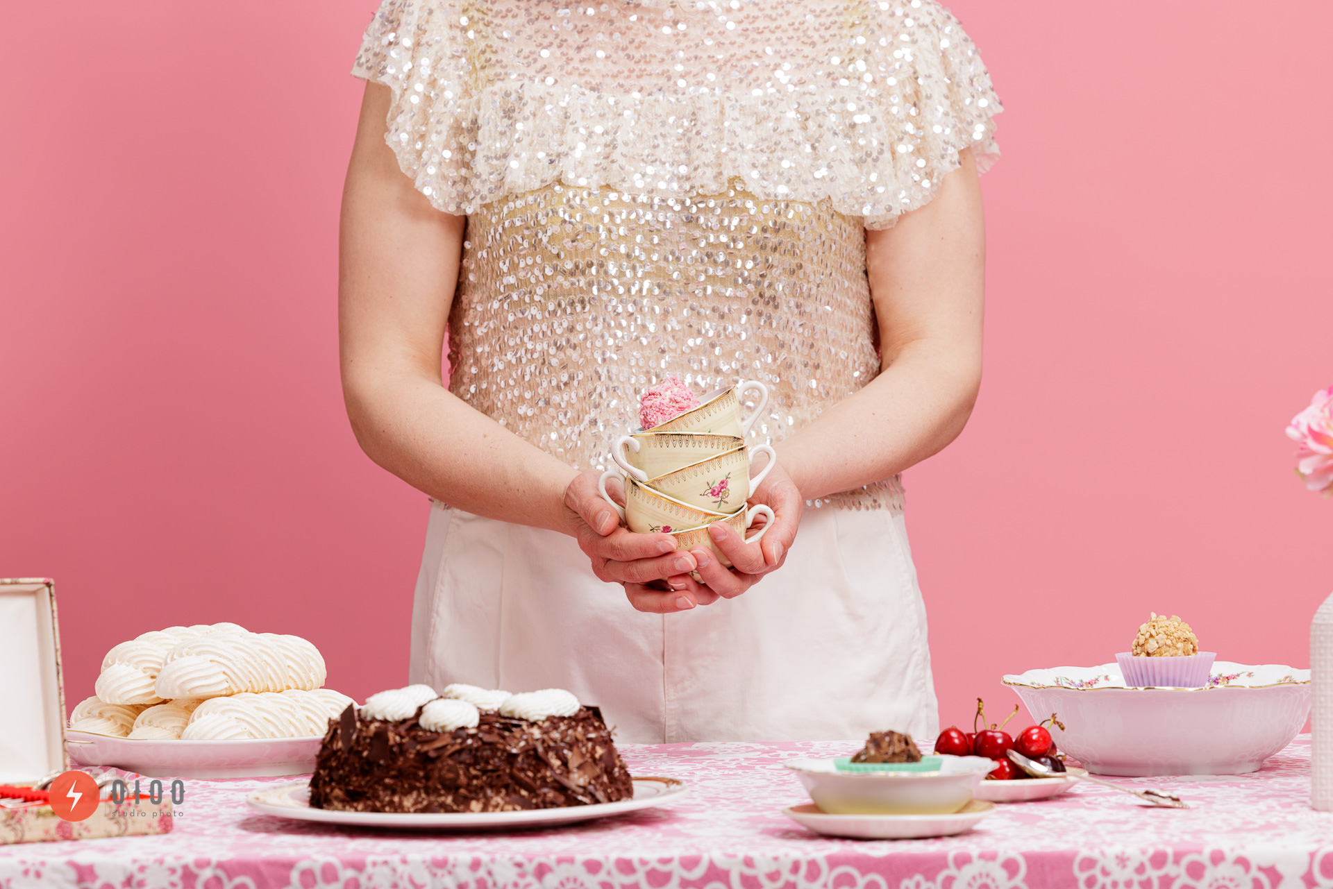 photos personal branding pour Sabine Rainard : une table est dressée, pleine de gateaux. Une femme est debout derrière la table et tiens un cupcake au creux de ses mains. On ne voit pas son visage. Le fond est rose.