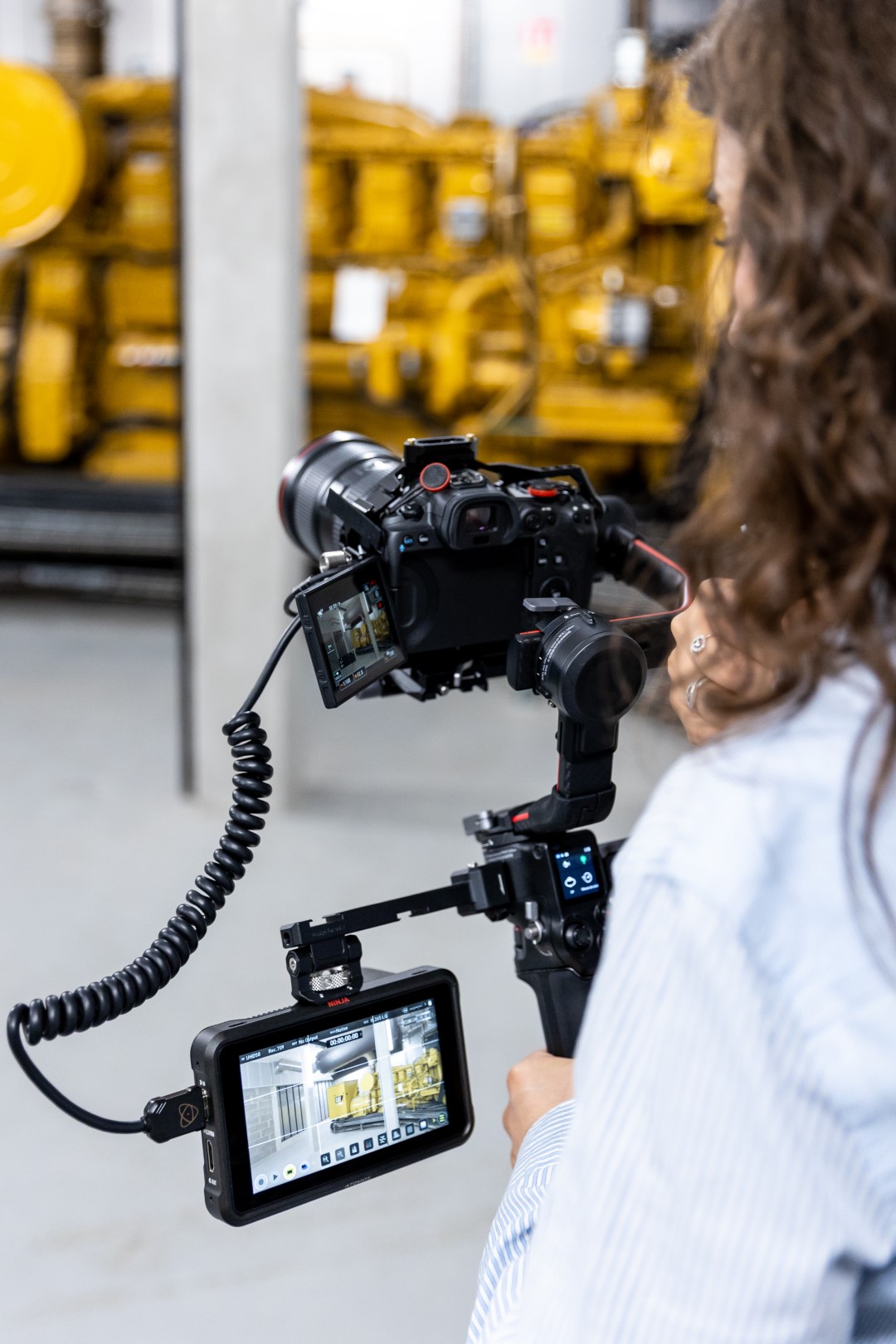 photo backstage d'une femme en train de tourner une vidéo d'entreprise à Nantes. Elle est de dos, et tiens une caméra professionnelles sur un gimbal avec un écran externe.